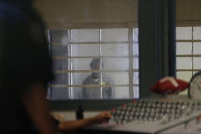 A prisoner behind bars and thick plastic looks over at a correction officer in an enhanced supervision housing unit on Rikers Island.